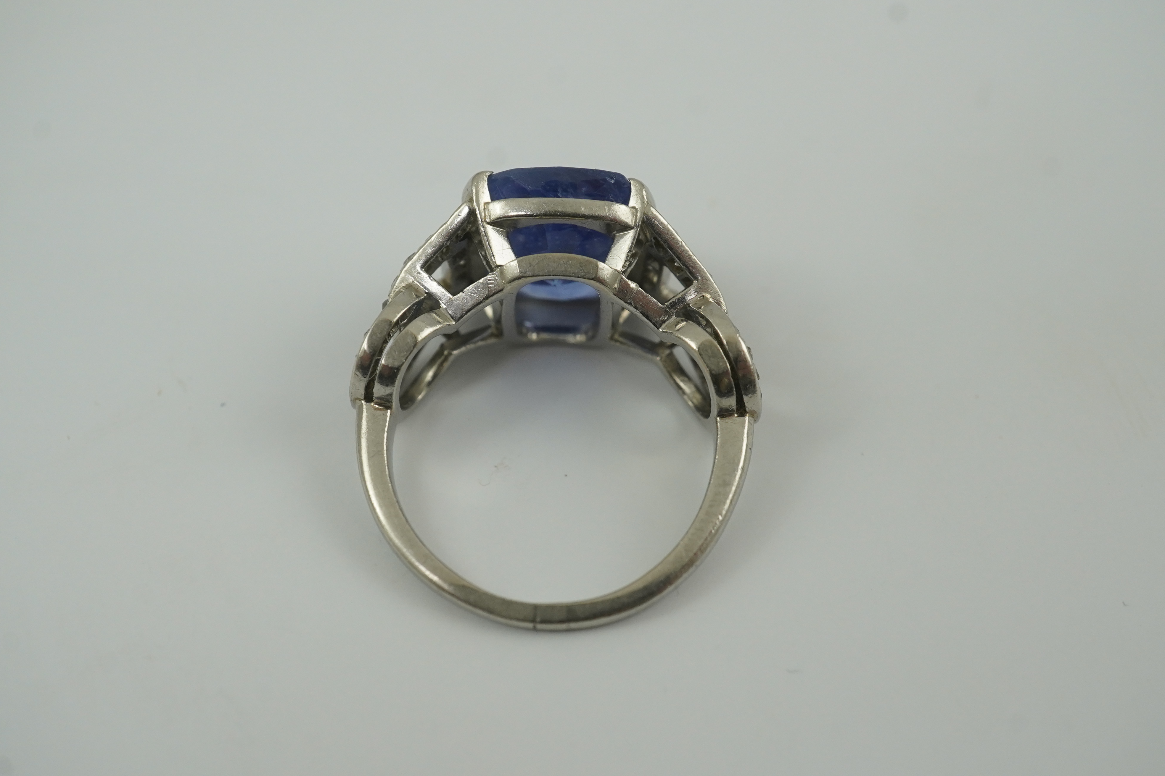 A mid to late 20th century platinum and single stone tapered cushion cut sapphire set dress ring, with diamond chip set pierced shoulders